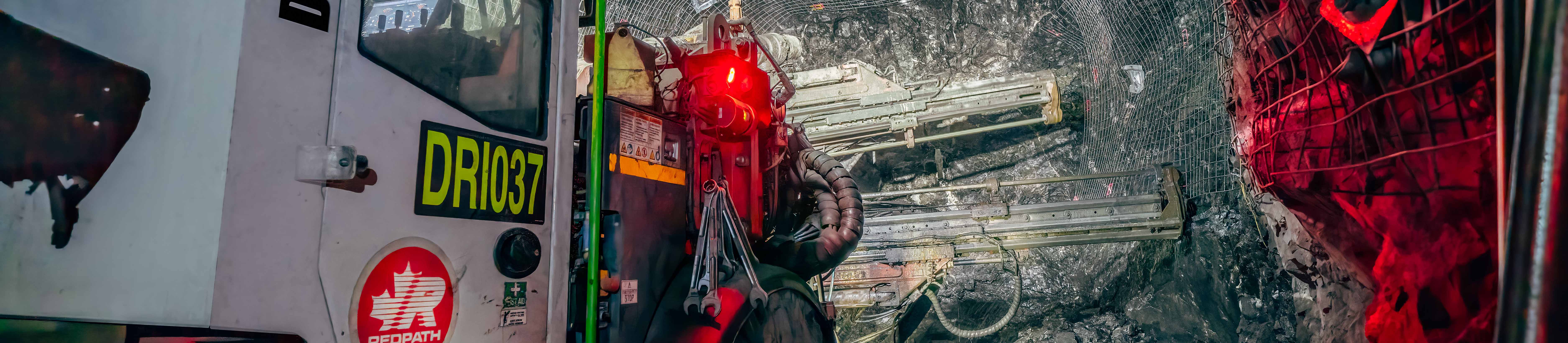 El banner del sitio web para la página de medios sociales muestra un taladro de pernos Redpath que aplica malla de alambre en las paredes y el techo de un túnel subterráneo.