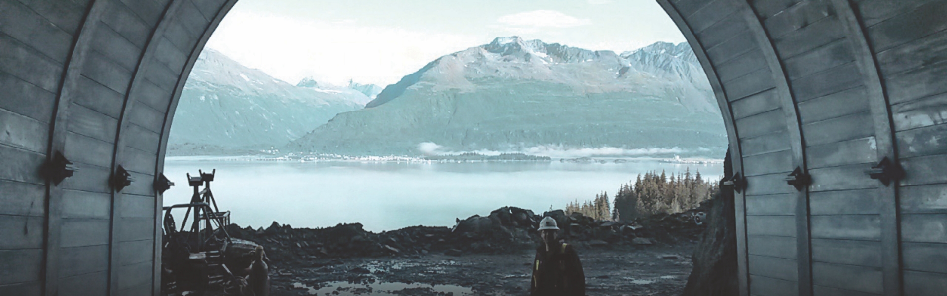 Une image d'un employé de Redpath debout au premier plan de l'ouverture d'un puits de mine, avec un paysage naturel en arrière-plan, qui comprend des montagnes, des forêts et un lac.