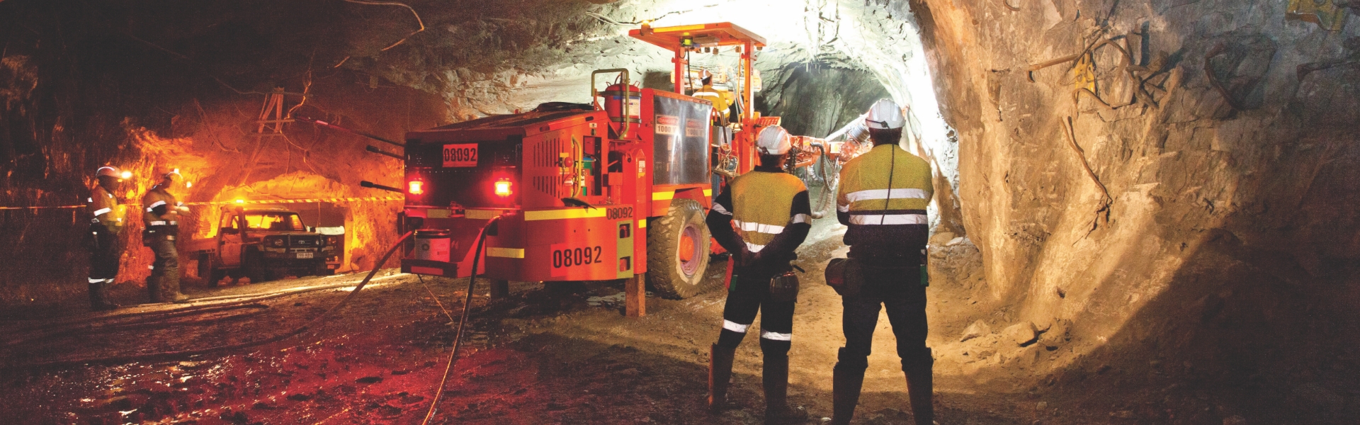 Redpath employees observing a jumbo machine performing lateral drilling in an underground tunnel.