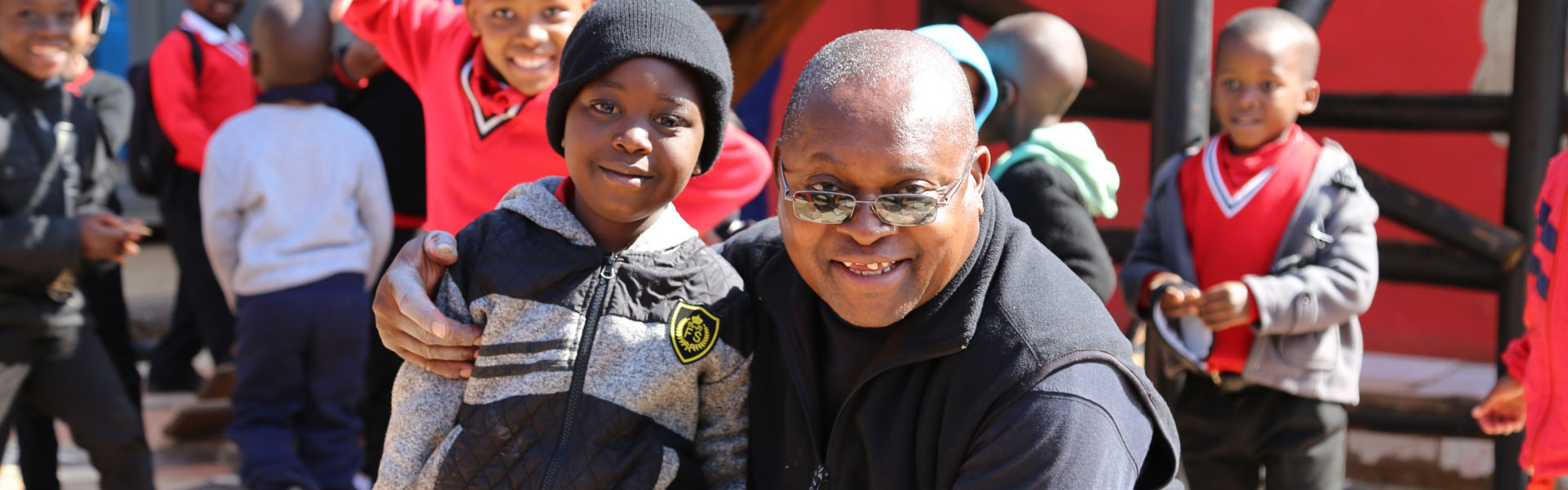 An image of a father and son posing for a photo at the MiniChess Programme, which uses chess as part of the school curriculum to teach basic maths, science, language and life skills to preschool and foundation phase learners.