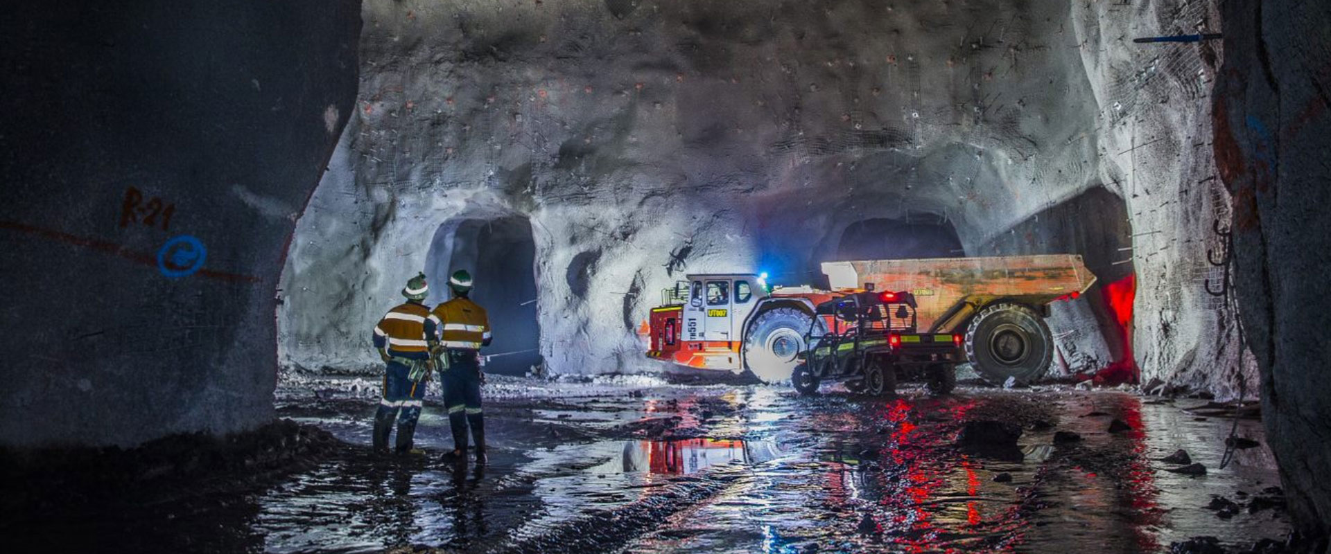 Redpath Mongolia employees having a discussion while standing next to heavy-duty machinery inside a giant excavated cavern.